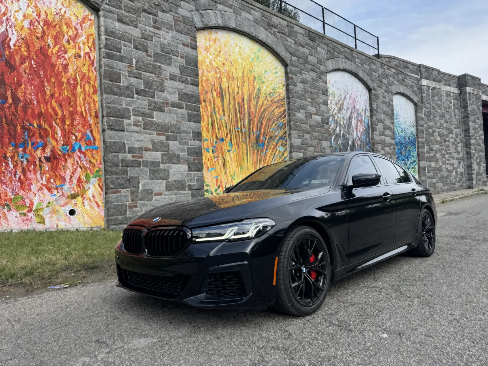 BMW 5 Series in factory gloss black paint before the satin wrap, parked by the mural wall