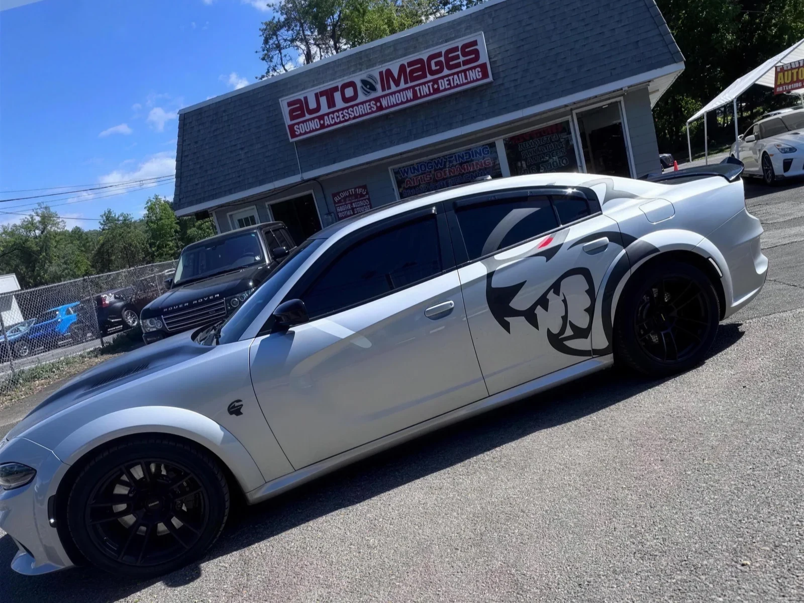 Silver widebody Dodge Charger Hellcat with tinted windows and a Hellcat side graphic at the shop