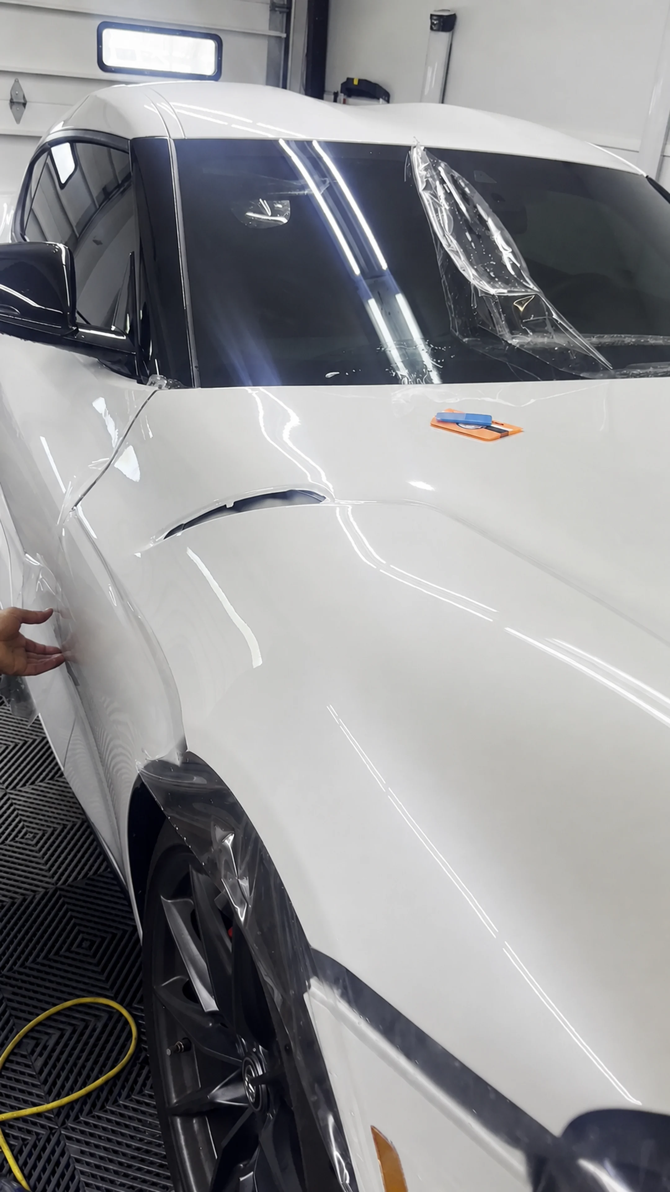 Wide in-progress view of clear paint protection film installation across the front of a white vehicle