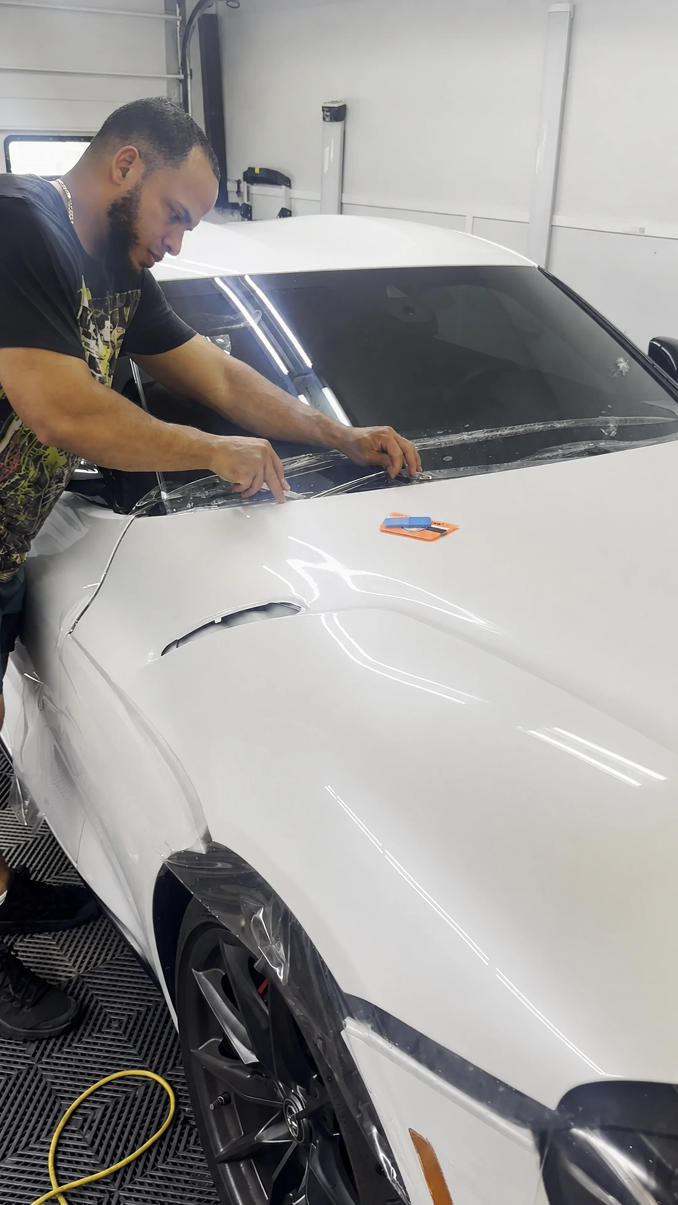 Auto Images installer positioning clear paint protection film across the hood of a white vehicle