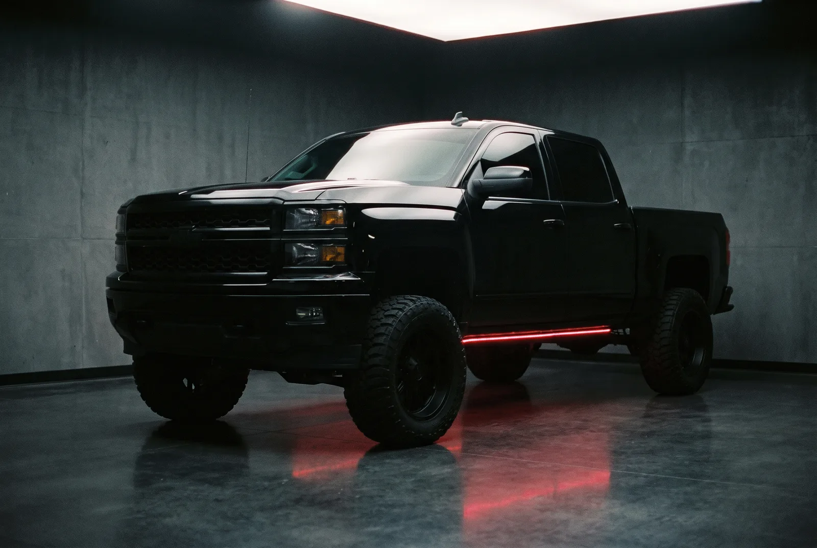 Lifted blacked-out pickup with red underglow in a dark studio