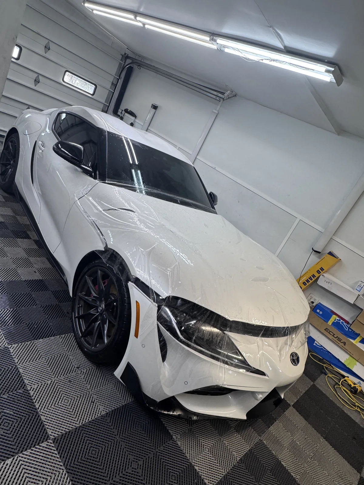 White Toyota GR Supra mid-way through paint protection film installation, film draped over the nose